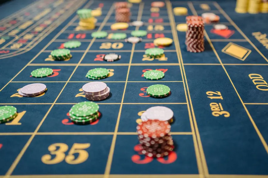 Close-up of a roulette betting layout on blue felt with stacks of green, white and red gaming chips placed across the numbers