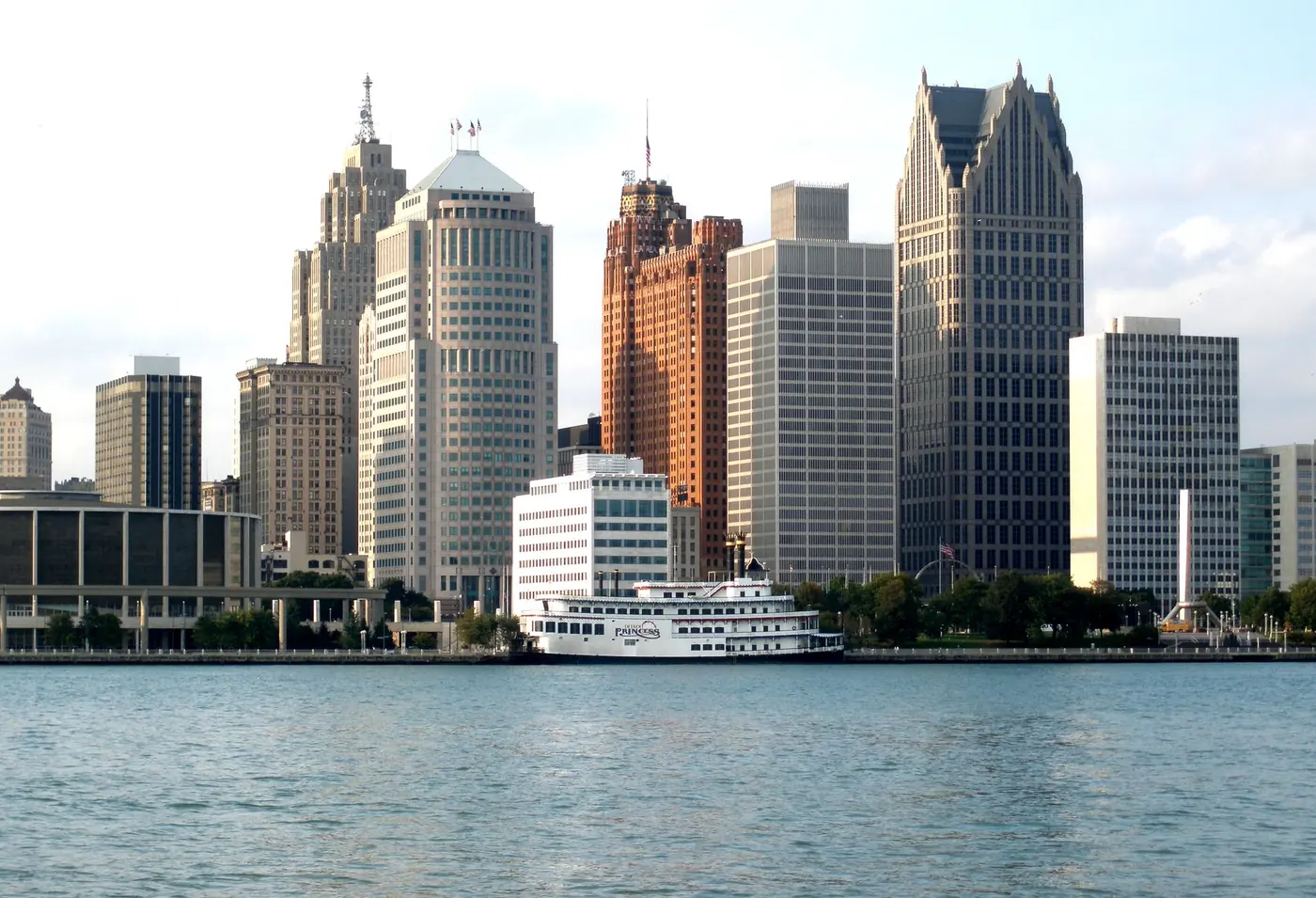 The skyline of a large North American city photographed across a wide river, with tall office towers and a moored riverboat on the far bank