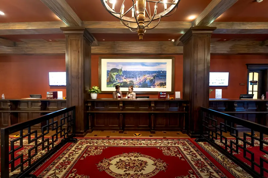 A hotel reception desk in a wood-panelled lobby with warm red walls, a patterned carpet and two staff members behind the counter