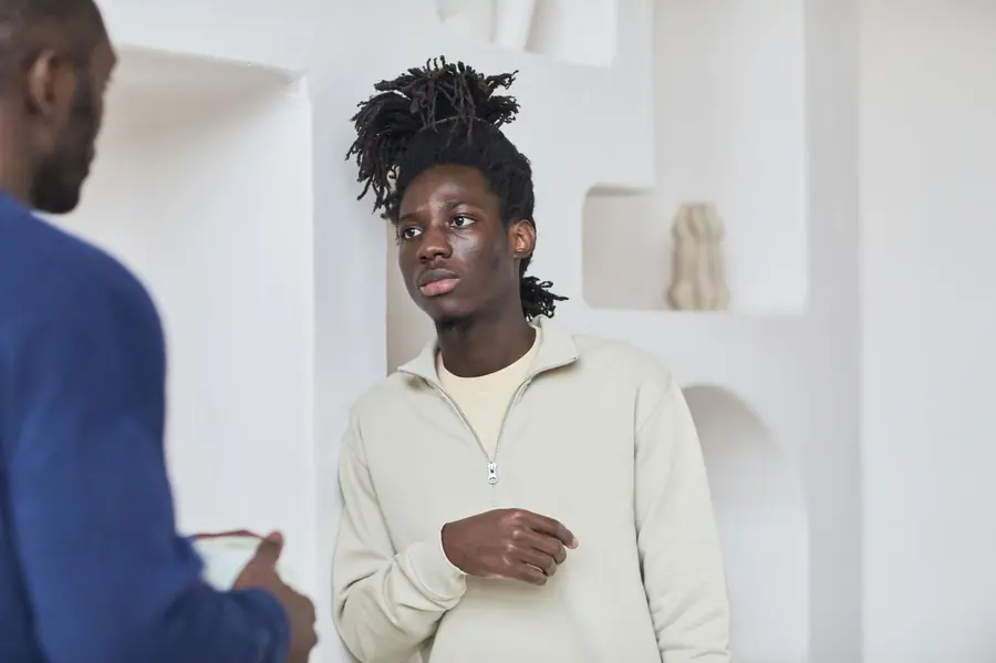 Two people standing in a bright room in conversation, one listening attentively to the other